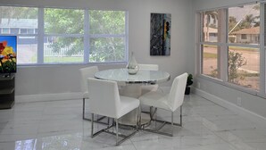 A modern dining area with a round table, four white chairs, a vase, and a painting on the wall.