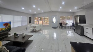A modern living room with a flat-screen TV, a coffee table, a sofa, and a dining area with a table and chairs.