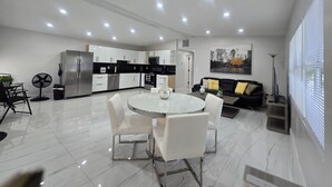 A modern kitchen with white cabinets, a dining area with a white table and chairs, and a black sofa with yellow cushions.