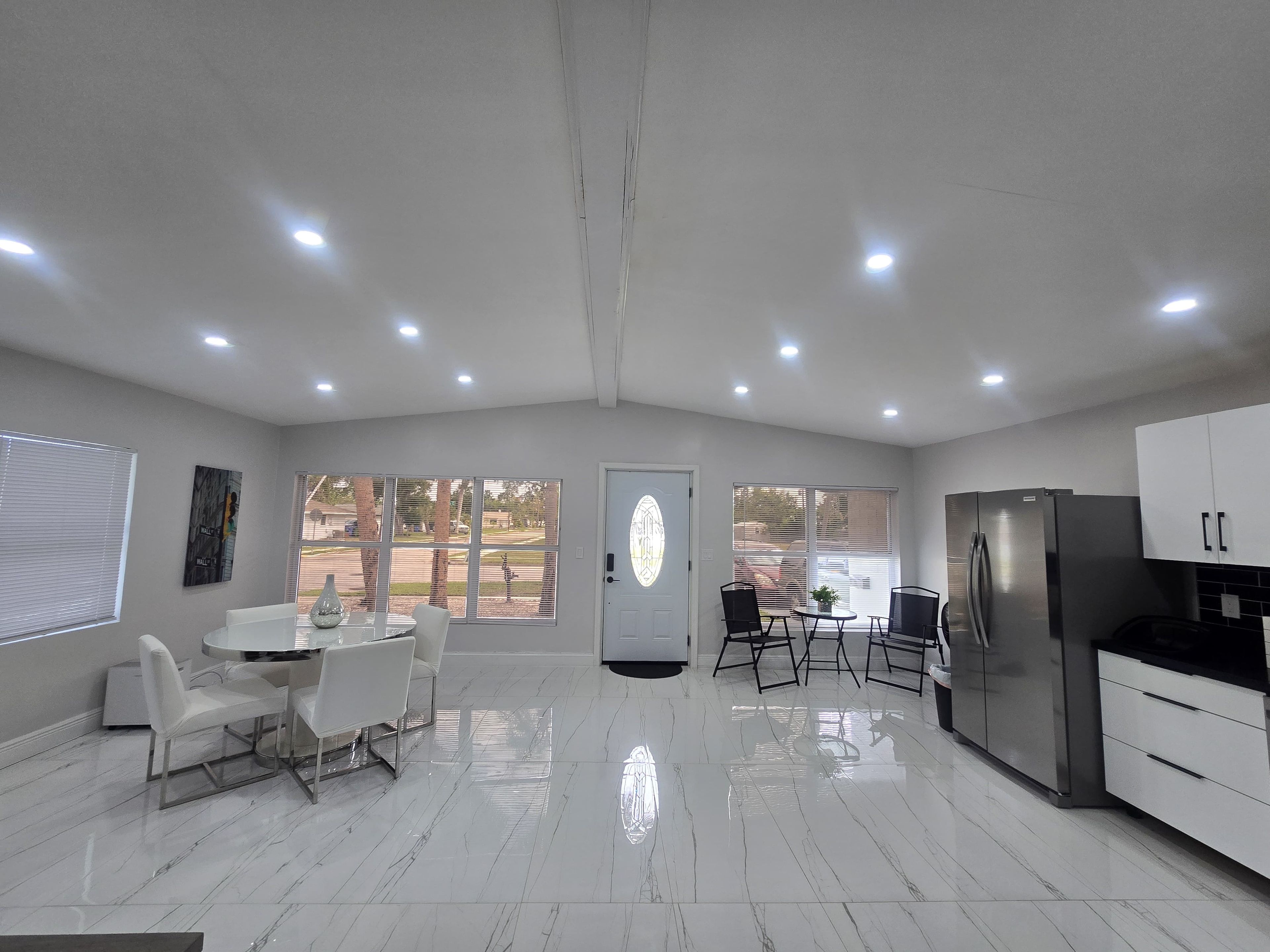 A modern kitchen with a refrigerator, cabinets, and a dining area with chairs and a table.