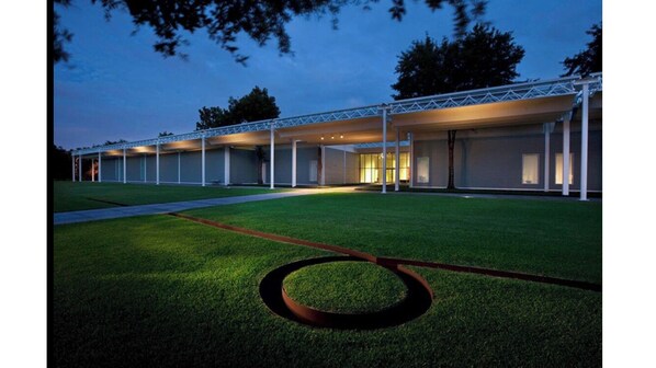 A modern building with a covered outdoor area, a well-maintained lawn, and a circular garden feature.