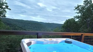 Ein Whirlpool auf einer Terrasse mit Blick auf einen bewaldeten Hügel.