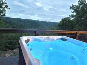 Ein Whirlpool auf einer Terrasse mit Blick auf einen bewaldeten Hügel.
