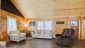 Ein Blockhaus-Interieur mit einer Couch, zwei Sesseln, einer Lampe und einer Tür mit einem Schild.