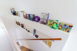 Uma escada com corrimão, uma prateleira com diversos objetos, incluindo livros, um brinquedo de pelúcia e uma caixa de lata.