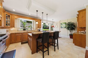 A kitchen with wooden cabinets, a central island, bar stools, pendant lights, and a view of the outdoors. - Spacious 4-bedroom house in delightful North Vancouver with AC (North Vancouver)