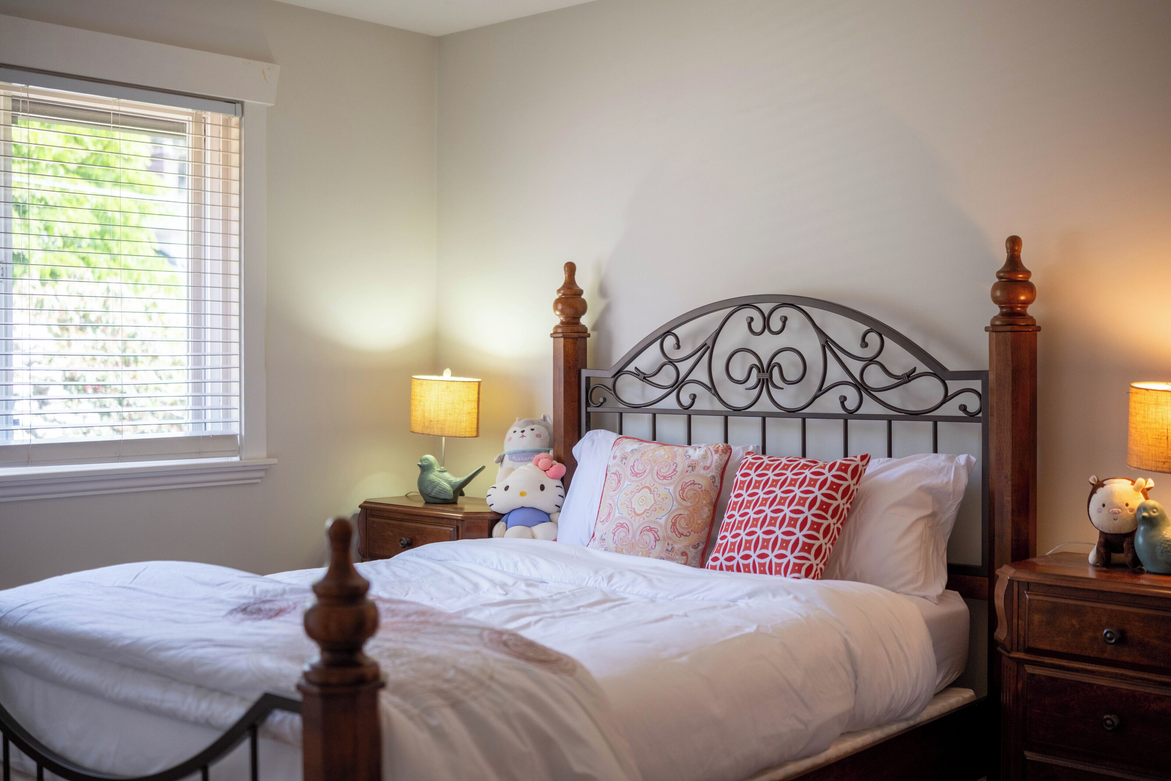A neatly made bed with a headboard, bedside lamps, and a window with blinds.