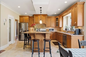 A kitchen with wooden cabinets, a central island with stools, stainless steel appliances, and a pendant light. - Spacious 4-bedroom house in delightful North Vancouver with AC (North Vancouver)