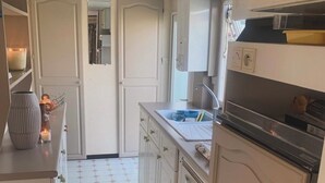 Una cocina estrecha con armarios blancos, piso de baldosas y un horno a la vista.