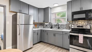 A modern kitchen with grey cabinets, stainless steel appliances, and patterned backsplash.