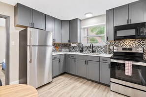 A modern kitchen with grey cabinets, stainless steel appliances, and patterned backsplash.