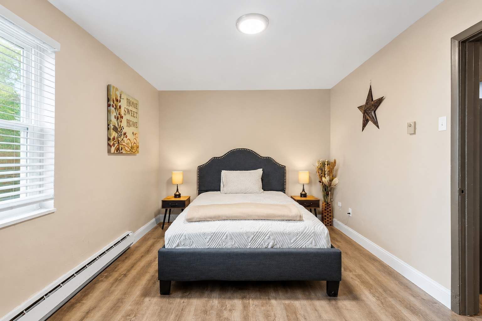 A bedroom with a bed, bedside tables, a star decoration, and a window with blinds.