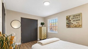 A bedroom with a bed, a dresser, a mirror, a window with blinds, and a wall decoration.