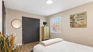 A bedroom with a bed, a dresser, a mirror, a window with blinds, and a wall decoration.