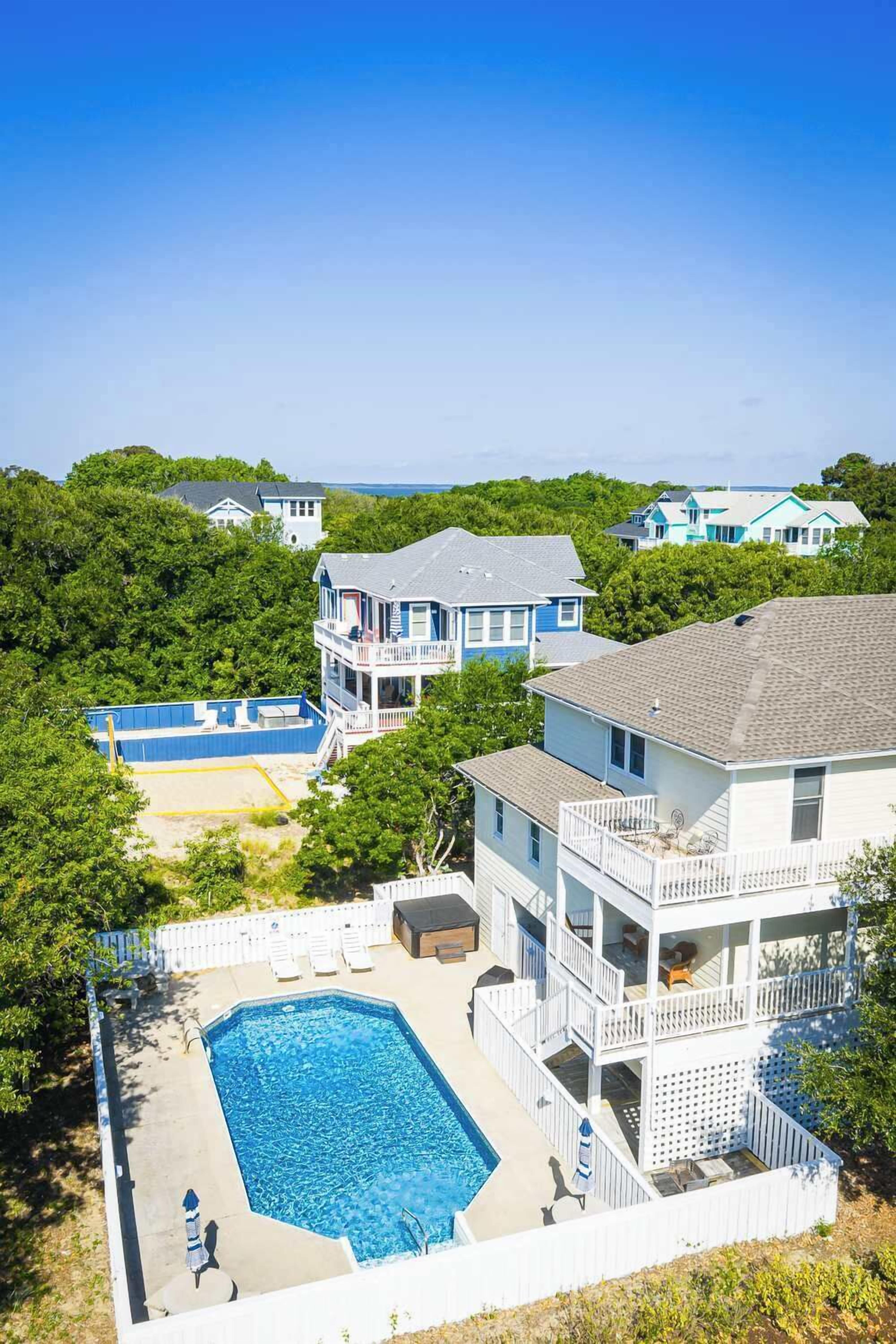 A large swimming pool surrounded by a white fence, with multiple buildings in the background.