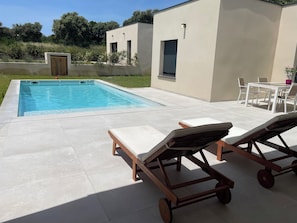 Uma piscina com espreguiçadeiras, uma mesa e cadeiras, rodeada por um espaço de terraço.