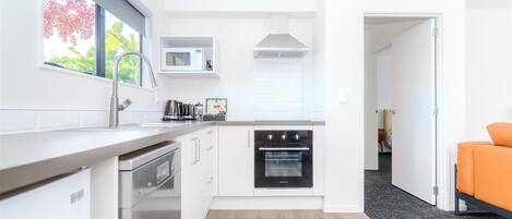 A modern kitchen with white cabinetry, a built-in oven, a microwave, and a window with a view of trees.