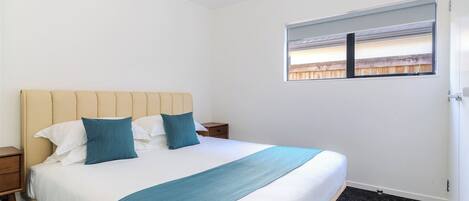 Quarto de hotel com cama, mesa de cabeceira, janela com persianas e porta.