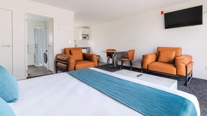 A hotel room with a bed, two orange armchairs, a small table, a TV, and a washing machine in the corner.