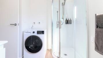Un baño pequeño con lavadora, ducha de vidrio y barra para toallas.