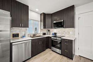 A modern kitchen with dark cabinetry, stainless appliances, and a tiled backsplash. - Cozy Apartment Near Marina | Boating & Hiking | Perfect Getaway (Coeur d'Alene)