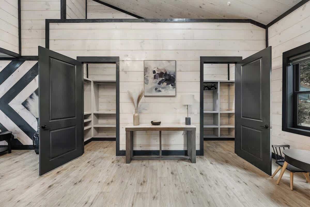A room with wooden walls and floors, a central bench, open shelves, and a painting on the wall.
