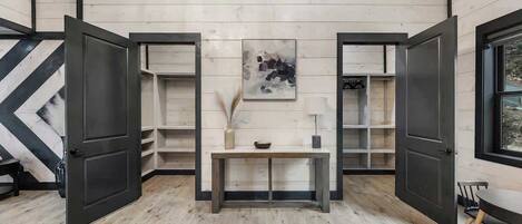 A room with wooden walls and floors, a central bench, open shelves, and a painting on the wall.