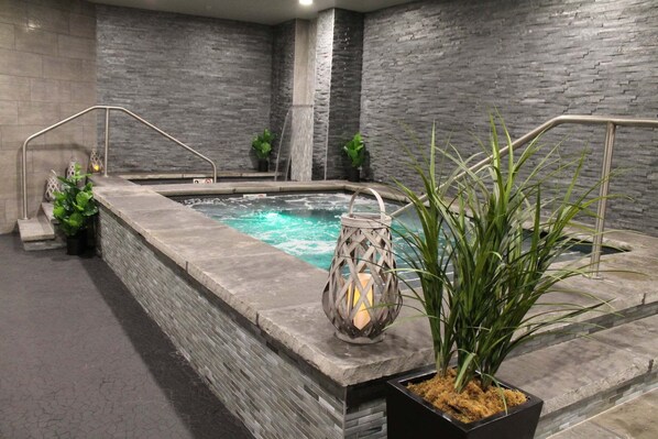 Een wellnessruimte met een jacuzzi, stenen muren, een metalen leuning en potplanten.