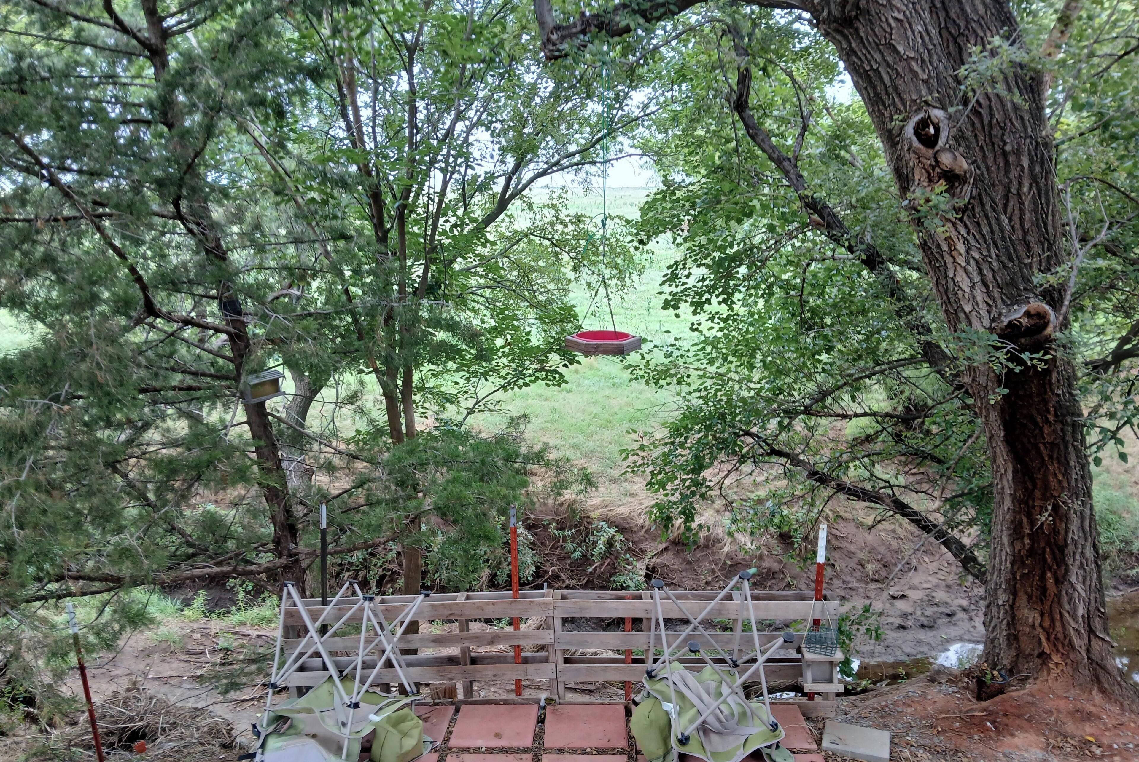 Un pont en bois doté d’un plancher à claire-voie, entouré d’arbres et surmonté d’un objet rouge suspendu.