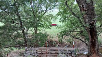 A wooden bridge with a grid floor, surrounded by trees and a red hanging object.