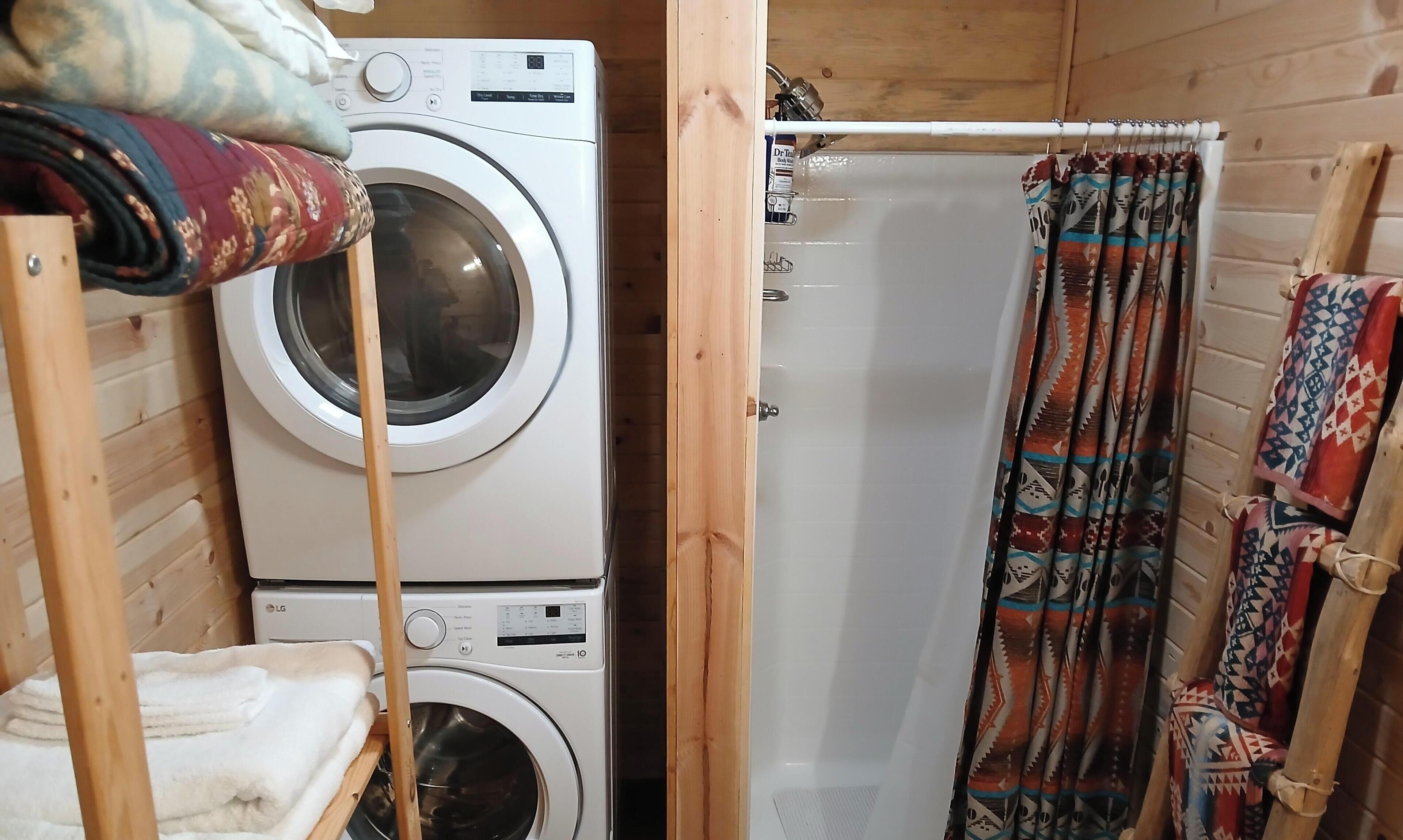 A compact laundry area with stacked washing machines, a shower curtain, and a wooden door.
