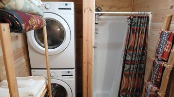A compact laundry area with stacked washing machines, a shower curtain, and a wooden door.