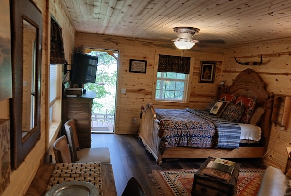 A wooden cabin interior with a bed, a television, a dining table, and a window.