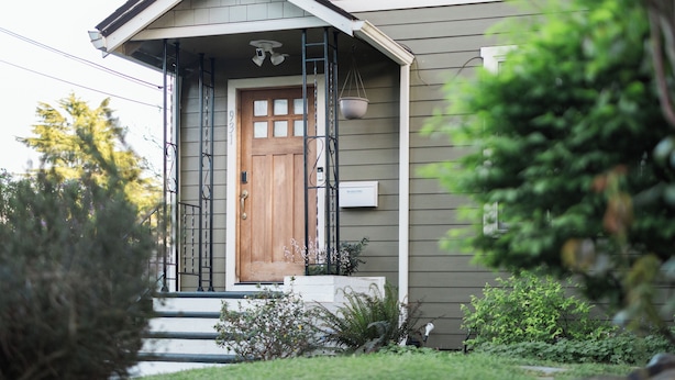 Una casa residenziale con una porta d'ingresso in legno, un piccolo portico e una fioriera pensile.