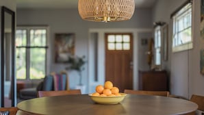 Un tavolo da pranzo con una ciotola di arance, sedie di legno e una lampada a sospensione con paralume intrecciato.