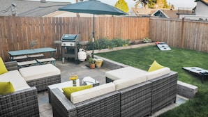 Un giardino sul retro con patio, mobili da esterno, un barbecue e un tavolo da ping pong.