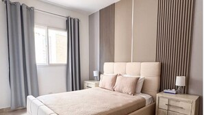 Un dormitorio con cama, mesitas de noche, cortinas y una ventana.