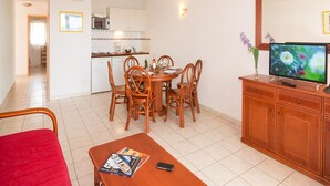 Un comedor con una mesa redonda y sillas, un televisor sobre un mueble de madera, y una silla roja.