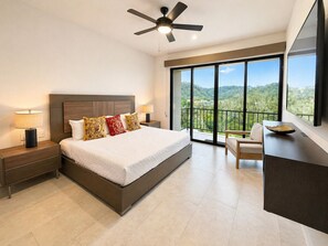 Ein Schlafzimmer mit Bett, Nachttischen, Schreibtisch, Stuhl, Deckenventilator und einem Balkon mit Blick.