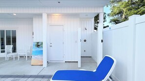 A covered outdoor seating area with a blue lounge chair, white walls, and a door with a beach scene mural. - Luxury private House + Pool. Walk to the beach (North Myrtle Beach)