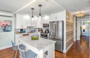 A modern kitchen with white cabinetry, stainless steel appliances, and a marble island. - Remodeled One BD Ocean, AC,wifi, pool, Luana Kai D202 (Kihei)