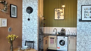 Een moderne keuken met een eethoek, met een ronde houten tafel, stoelen, een kroonluchter en een wasmachine.