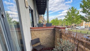 Een balkon met een stoel, plantenbakken en uitzicht op een woonwijk.