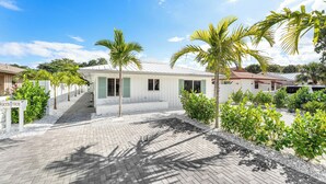 A residential property with a paved driveway, palm trees, and a white building with a red roof.