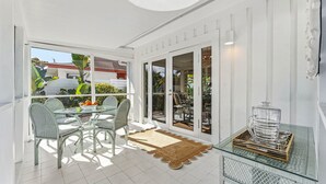 A sunlit patio with a glass table, chairs, and a woven doormat.