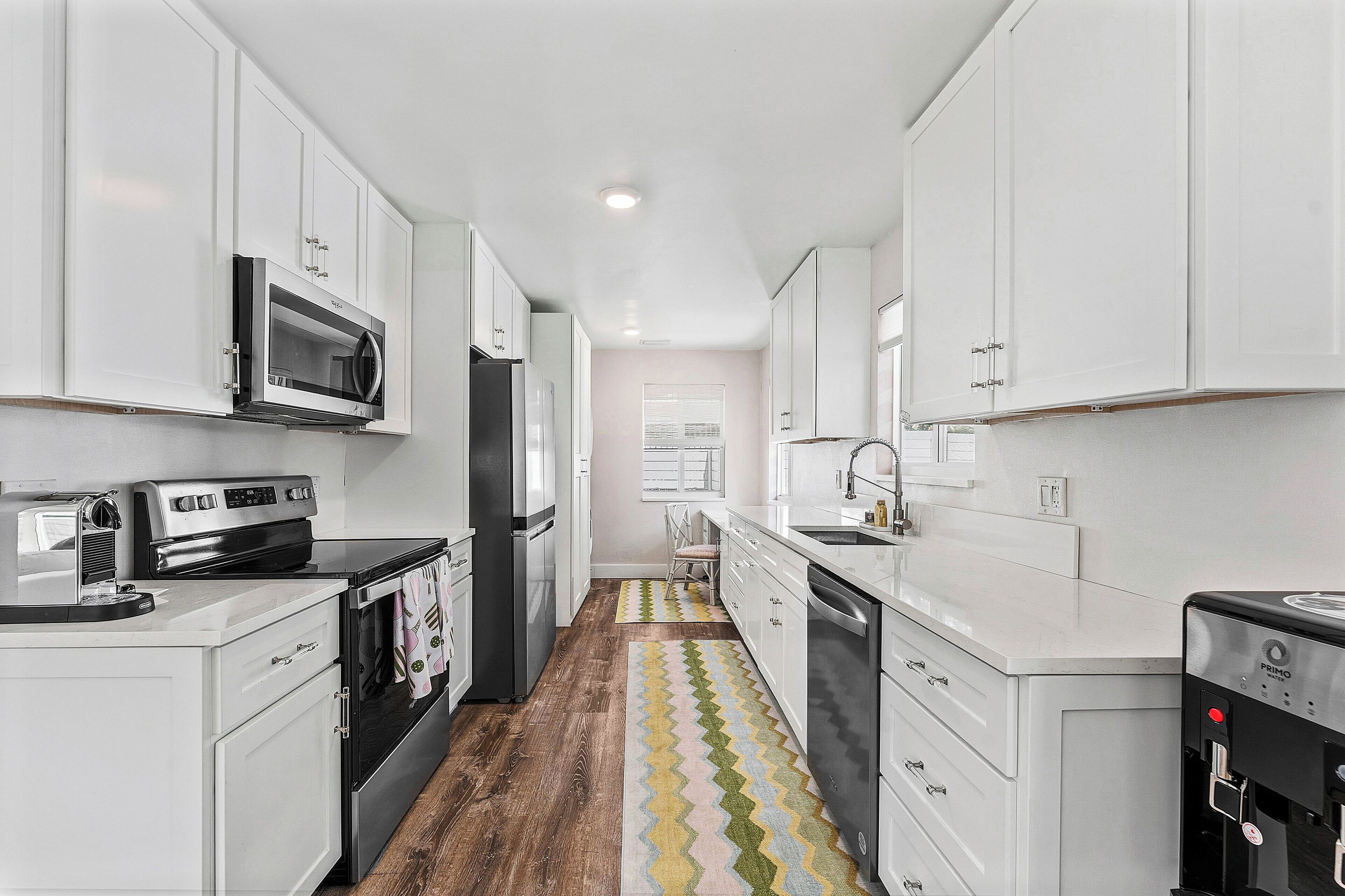 A narrow kitchen with white cabinets, a microwave, a stove, and a water dispenser.