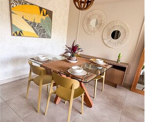 A dining area with a glass table, four chairs, a central plant, and decorative wall art.