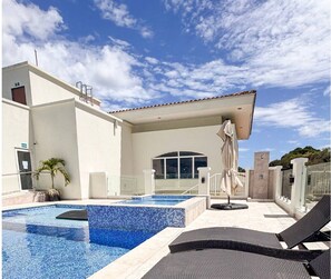 A modern pool area with a clear blue pool, lounge chairs, and a covered seating area.