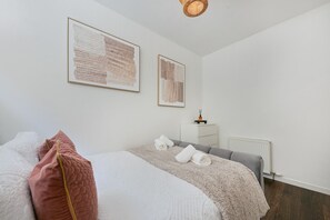 Une chambre à coucher avec un lit, des oreillers, une table de chevet, un radiateur et deux œuvres d’art encadrées accrochées au mur.