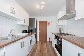 A compact kitchen with a washing machine, a coffee maker, a stove, and a sink. - Bon Accord Suite - Grampian Lettings (Aberdeen)